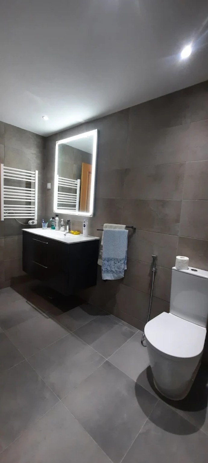 Casa de banho cinza com móvel escuro e espelho iluminado